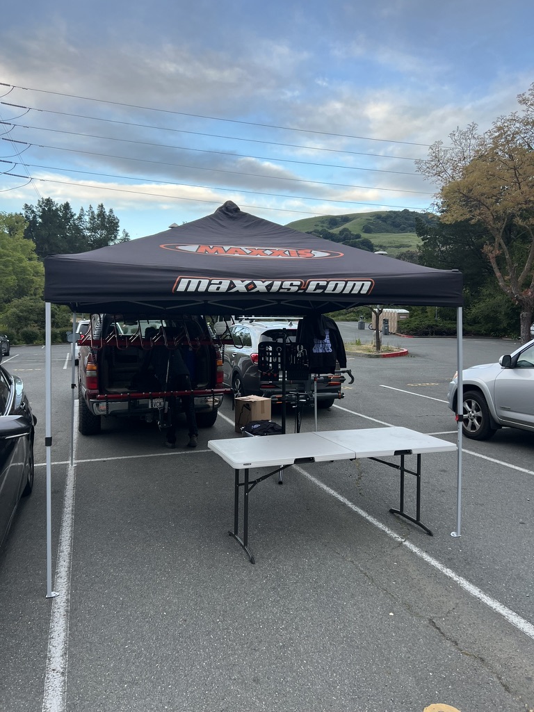 A Maxxis-branded canopy with a table, support vehicles and cycling supplies
