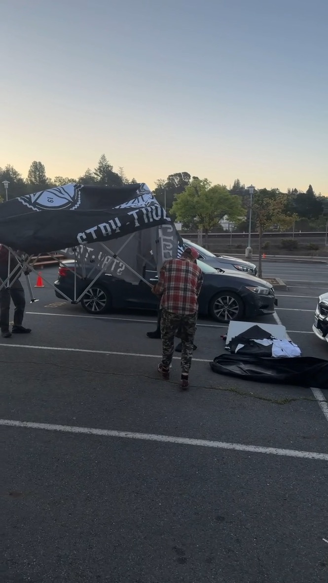 People raising the Stay True Cycles canopy beside parked vehicles