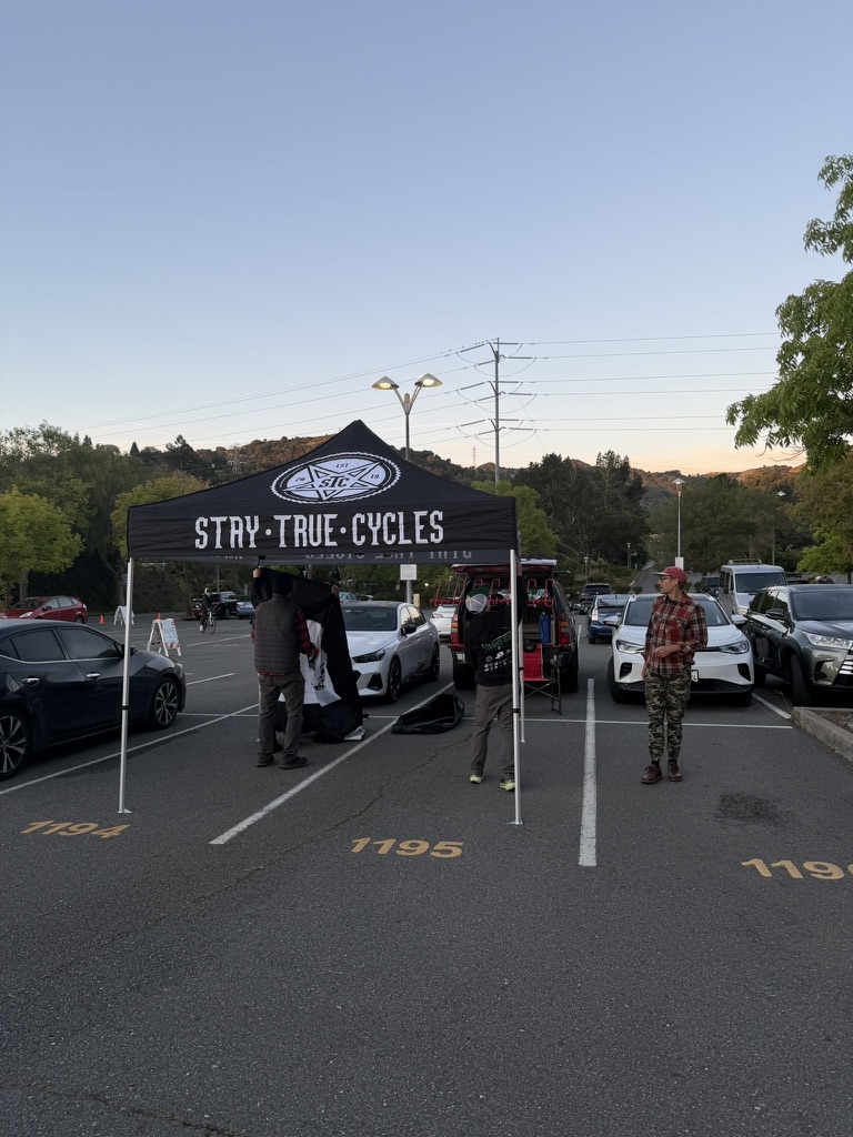 Stay True Cycles canopy with people and support vehicles in a parking lot