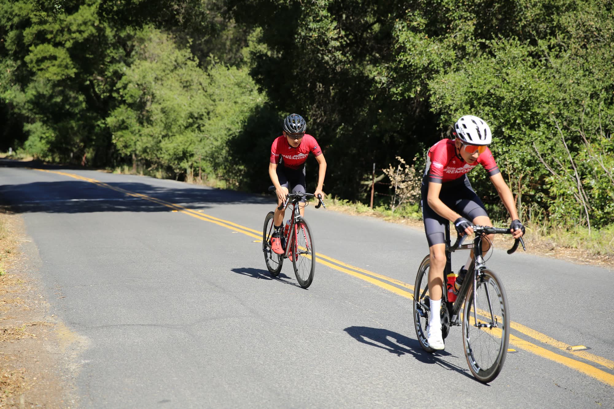 Two junior riders in red kits riding up a quiet road