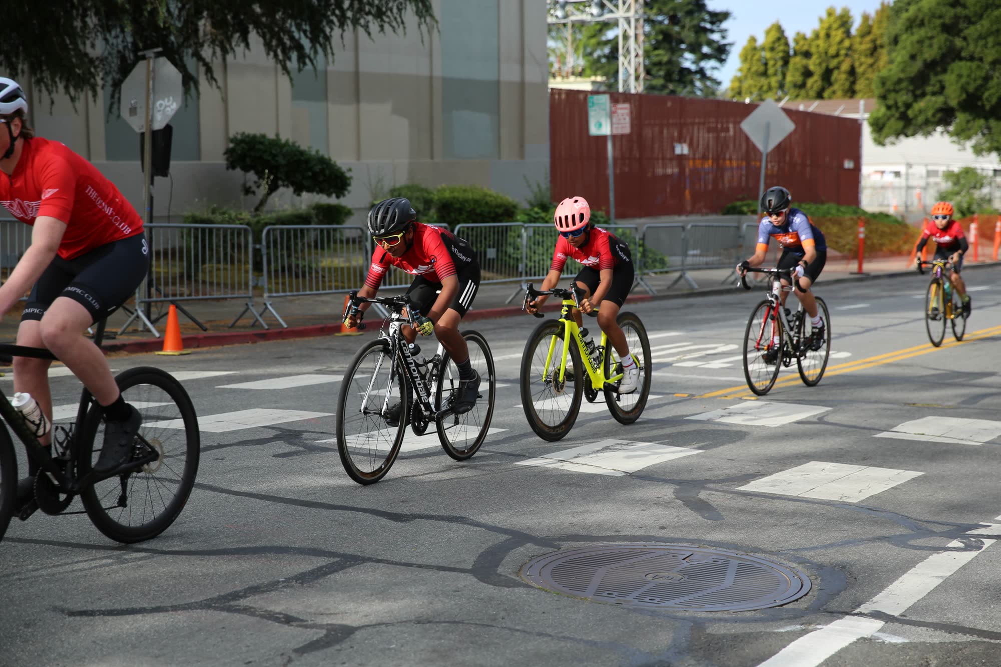 Junior riders in red and colorful kits riding through a downtown street with crosswalks and barriers