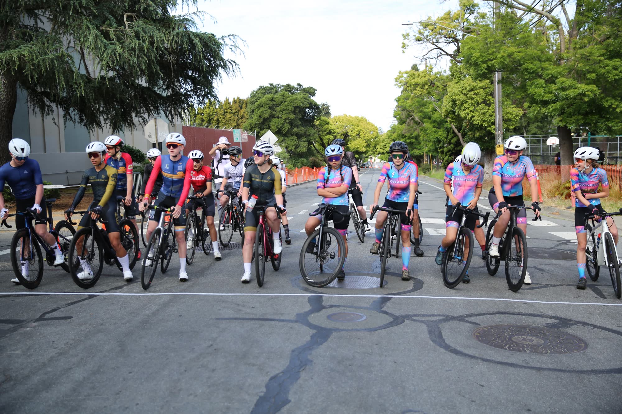 A large group of junior riders lined up at the start on a downtown street