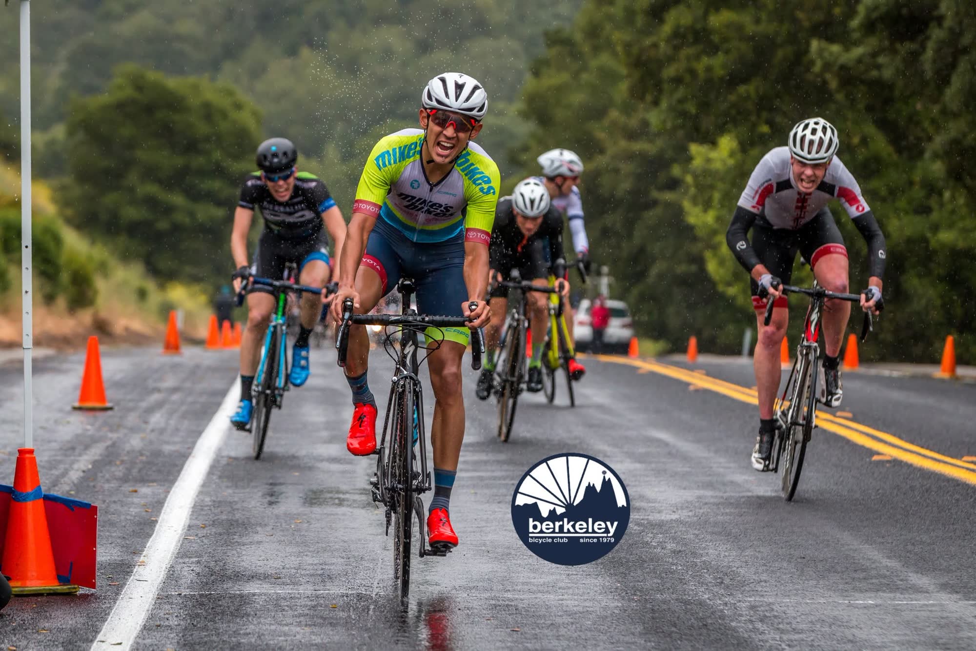 A rider grinning as they sprint toward the line on a wet road, with riders close behind