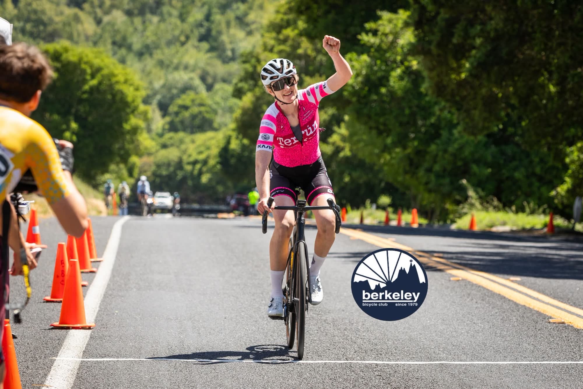 A rider in a pink kit raising a fist as they cross the finish line