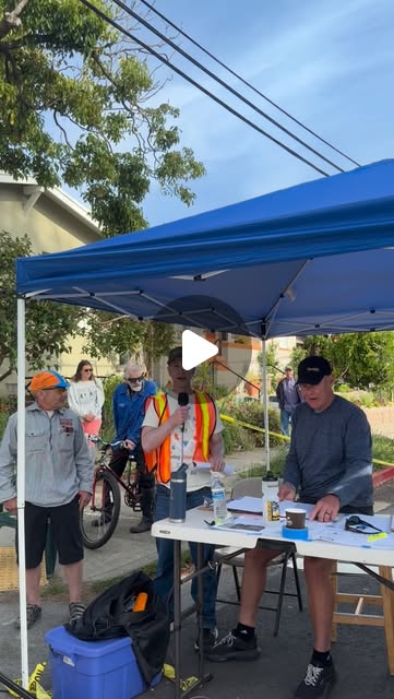 A man in a safety vest speaking into a microphone under a blue canopy at the 2026 Berkeley Omnium