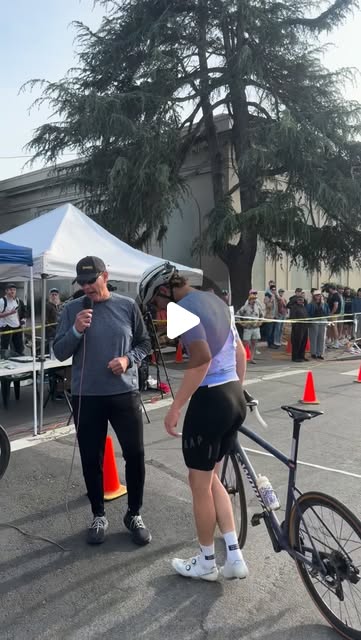 The announcer interviewing a rider on the course at the 2026 Berkeley Streets race, with spectators behind the barrier tape