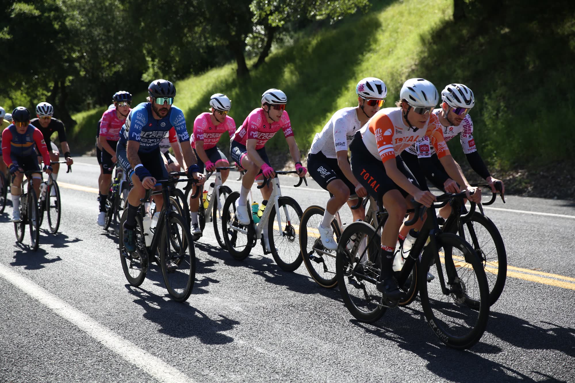 A tight group of riders in team kits, many in pink, on the Berkeley Hills Road Race course