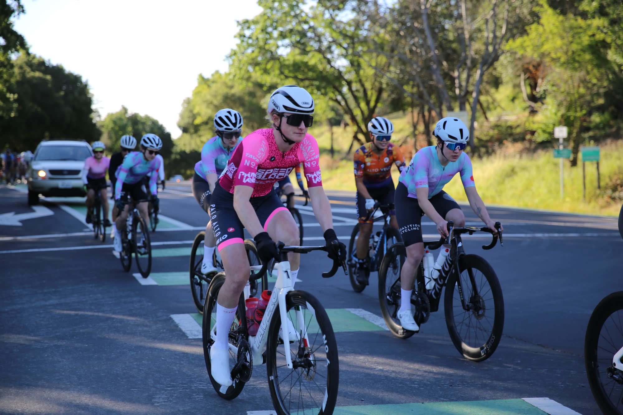 Riders in pink and light blue kits on a road with green bike lane markings at the Berkeley Hills Road Race