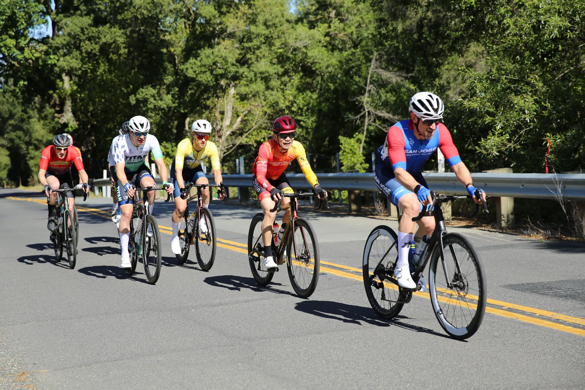 Five riders spread out along a road beside a guardrail at the Berkeley Hills Road Race