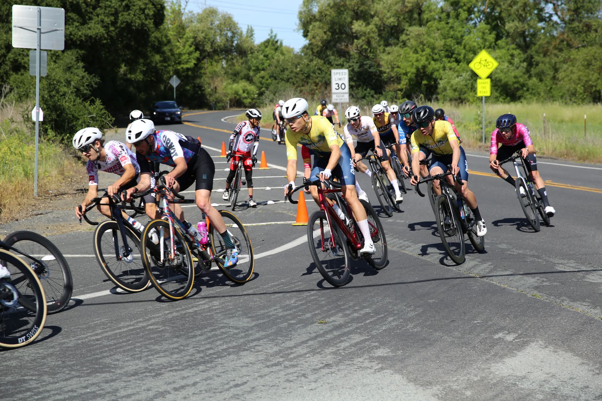 A group of riders leaning through a tight turn near a 30 mph sign at the Berkeley Hills Road Race