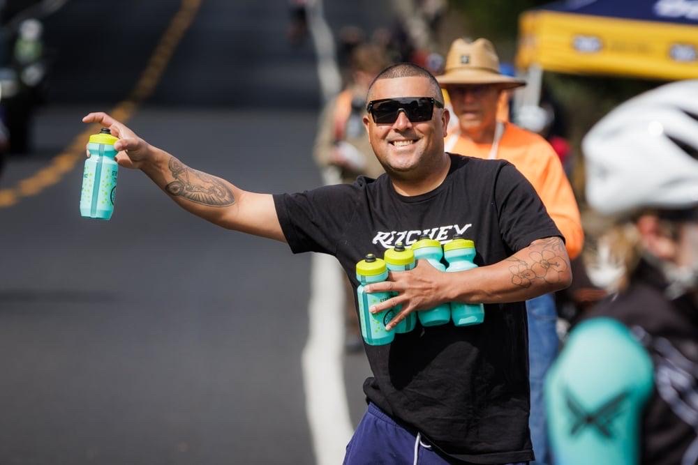 A smiling volunteer handing up water bottles at a feed zone