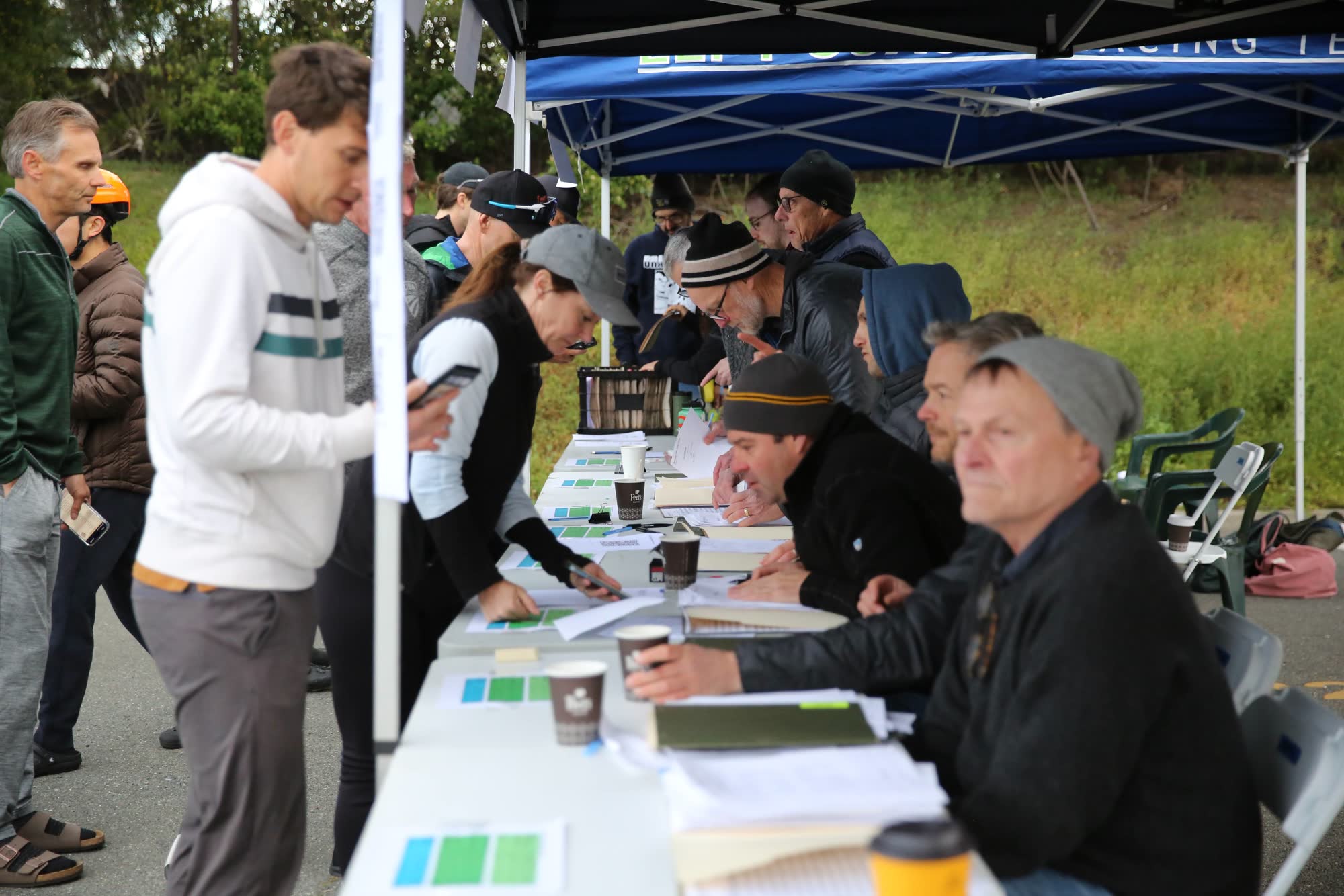 Volunteers and racers filling out forms at a sign-in table under a canopy