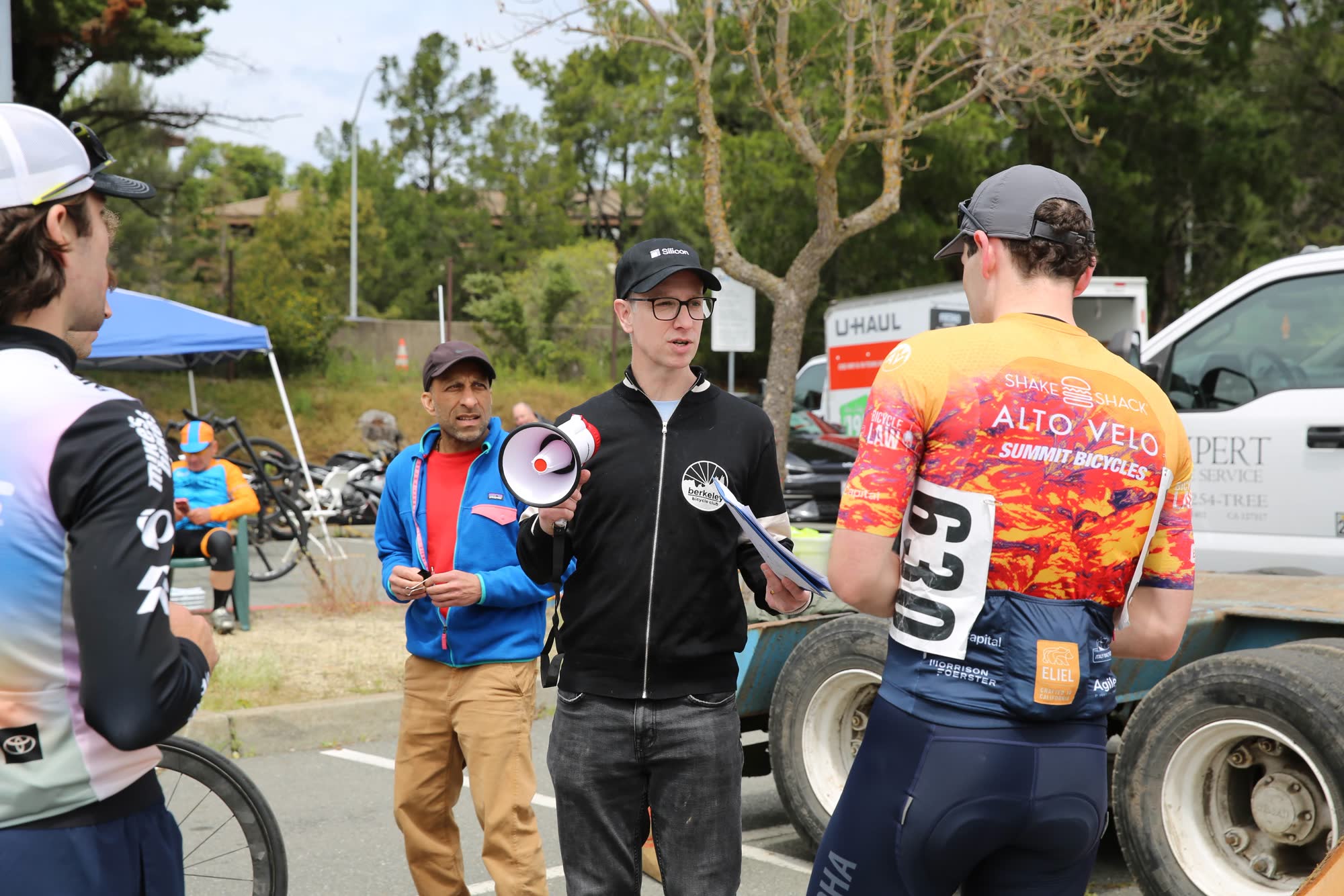 A race official with a megaphone briefing riders beside a truck
